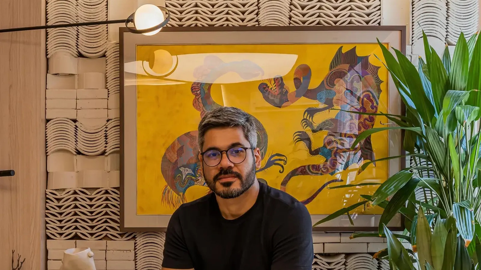 O arquiteto Arthur Braün no ambiente que assinou na CasaCor Ceará 2023, diante da parede de peças cerâmicas empilhadas